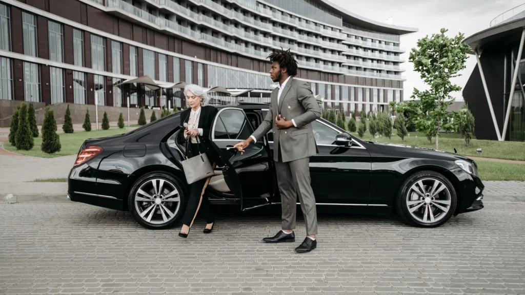 Chauffeur helping a passenger out of a black car outside a building