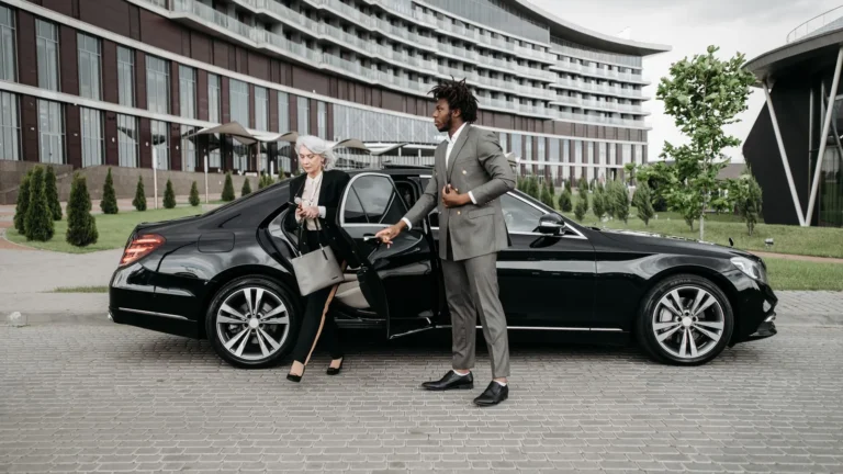 Chauffeur helping a passenger out of a black car outside a building