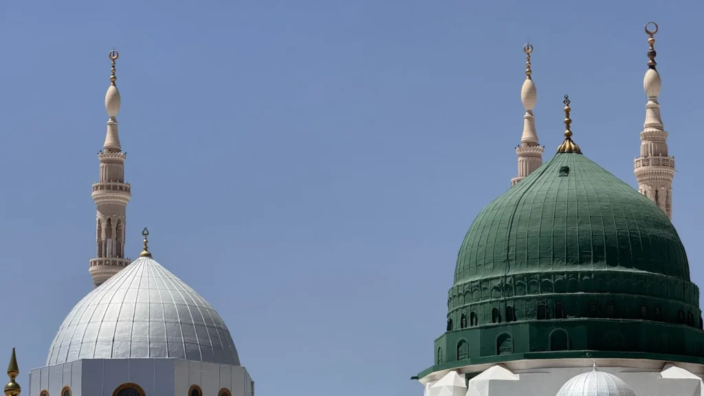 Green and silver domes of the Prophet's Mosque in Madinah under a clear sky