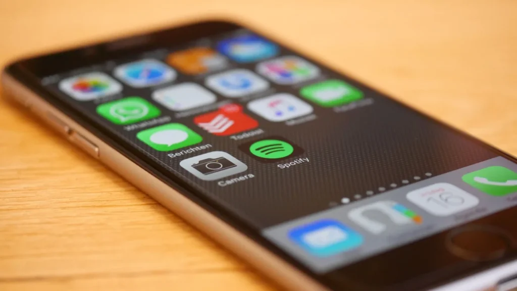 Smartphone lying on a wooden table with its home screen of apps