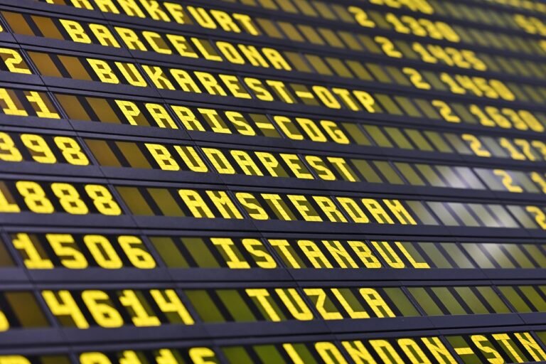 Pilgrims checking a flight departure board while planning a multi-leg journey that includes a stopover before Umrah