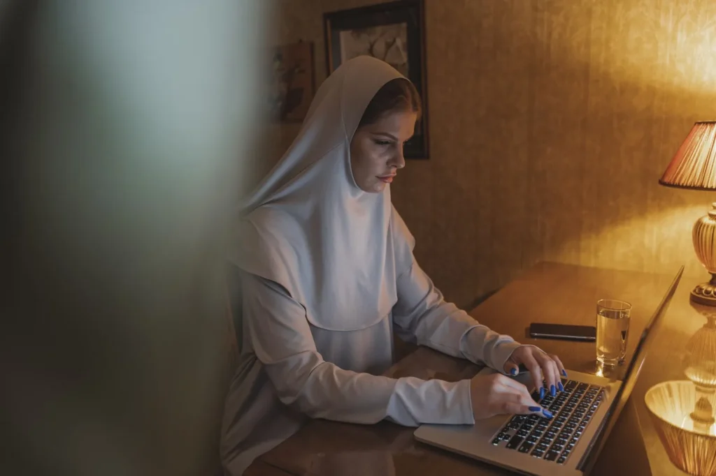A woman in a hijab working on a laptop at a desk in a warmly lit home office
